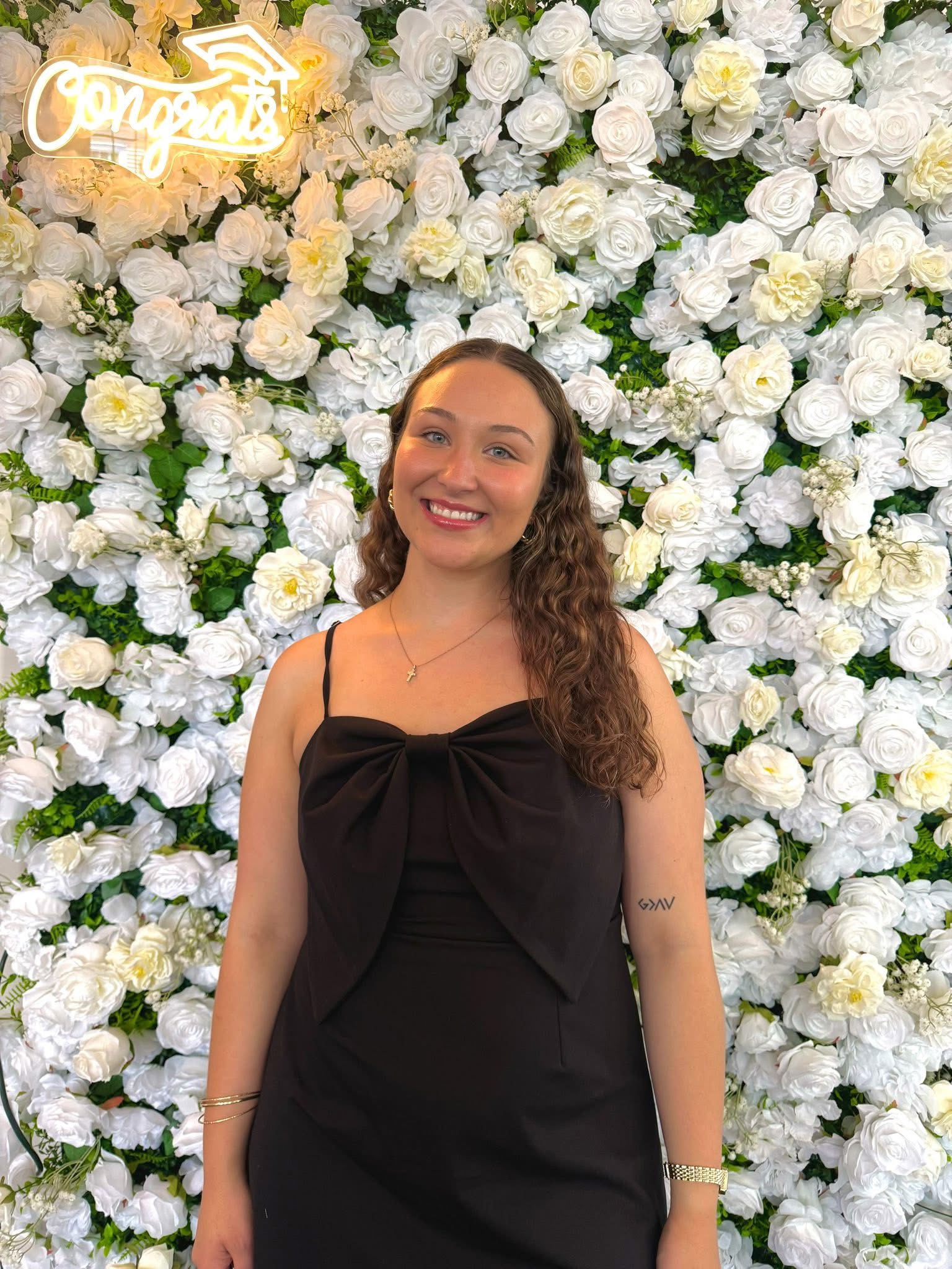 Single girl smiling in front of wall of white flowers